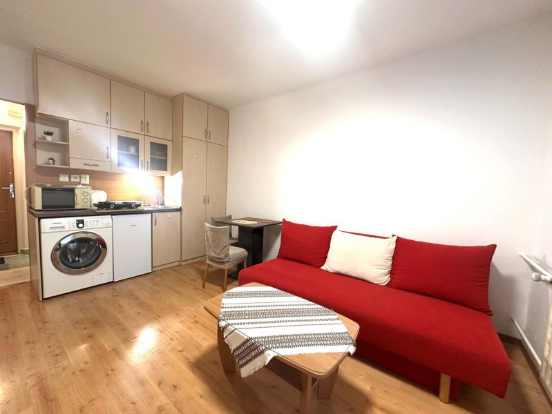 Ferienwohnung mit rotem Sofa, Kochnische und Boden mit Holzdekor.