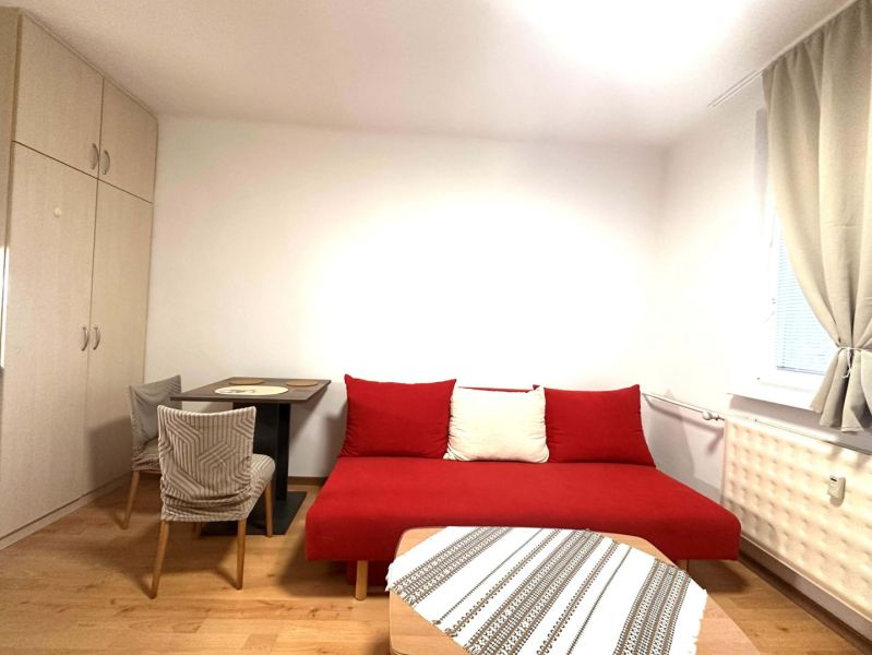 Ein Zimmer in einer Ferienwohnung mit einem roten Sofa, einem Tisch und einem Boden in Holzoptik.