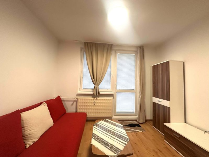 Ferienwohnung mit rotem Sofa, Holzboden-Dekor und Schrank mit Holzdekor.