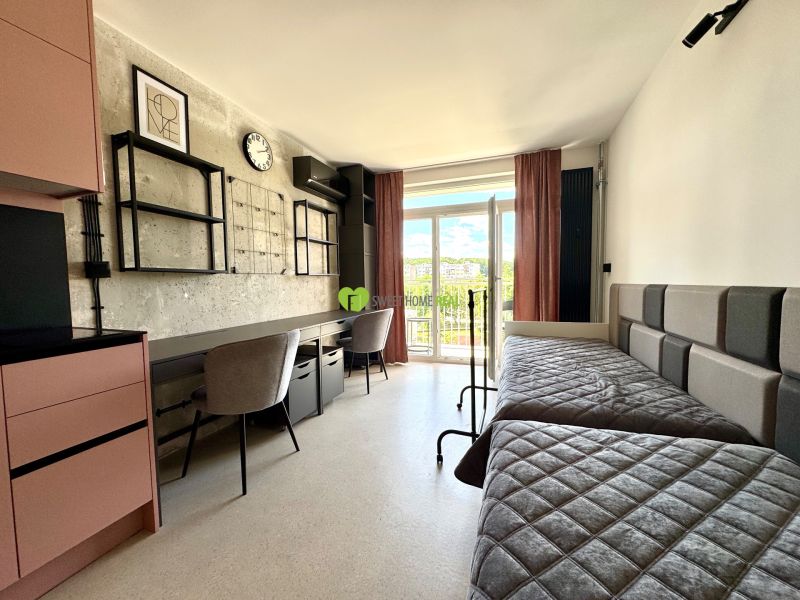 Einzimmerwohnung mit Betten, Schreibtischen, modernem Dekor und Blick auf den Balkon.