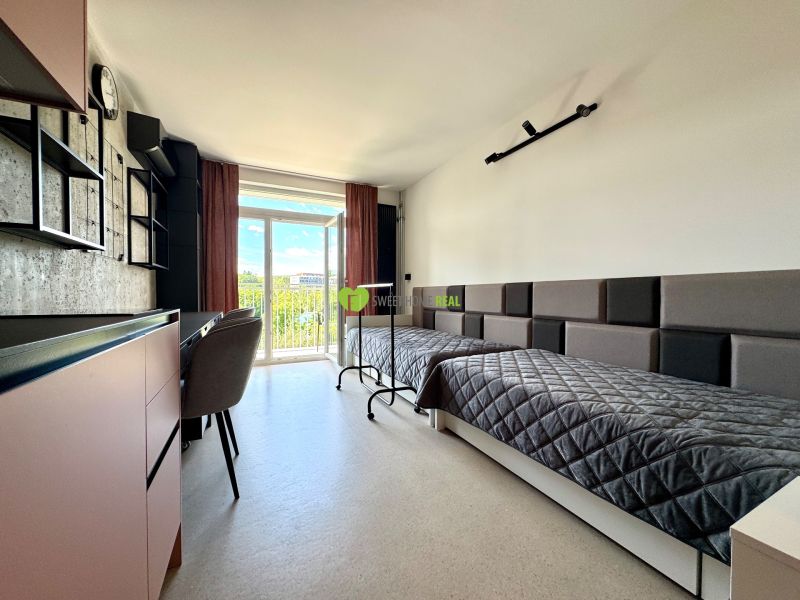 Einzimmerwohnung mit zwei Betten, einem Schreibtisch und Blick durch ein großes Fenster.