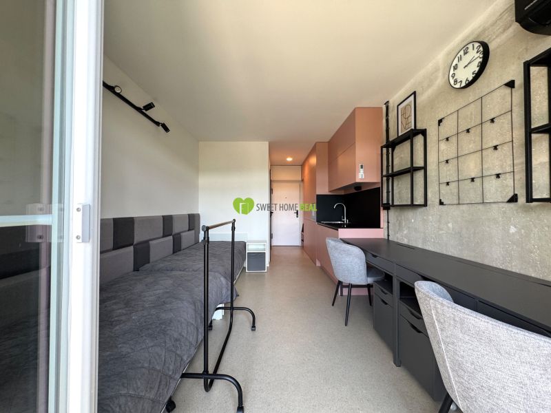 Innenraum eines Studios mit Bett, Tisch und Küchenzeile in sanften Farben.