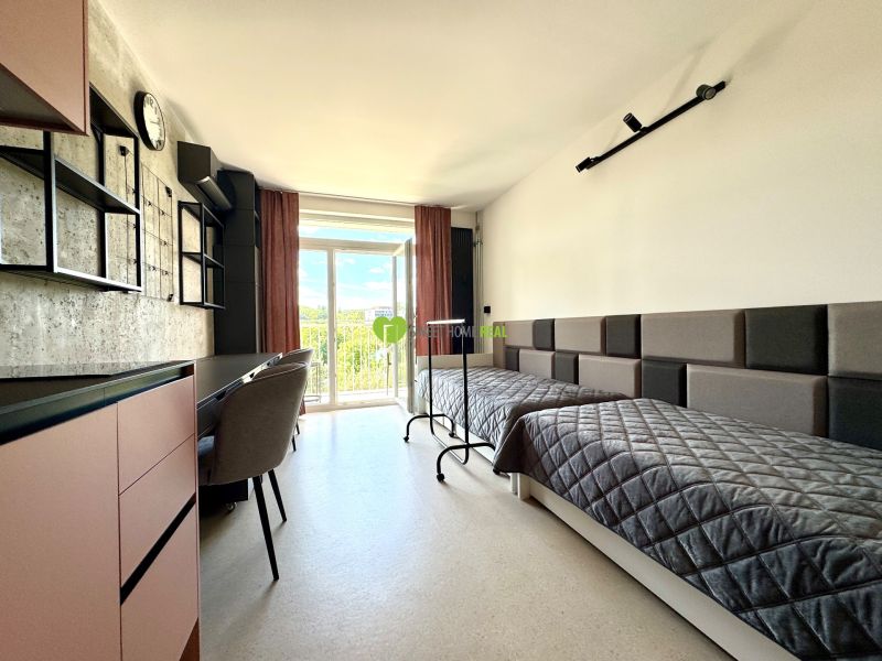Einzimmerwohnung mit zwei Betten, einem Schreibtisch und Blick durch ein großes Fenster.
