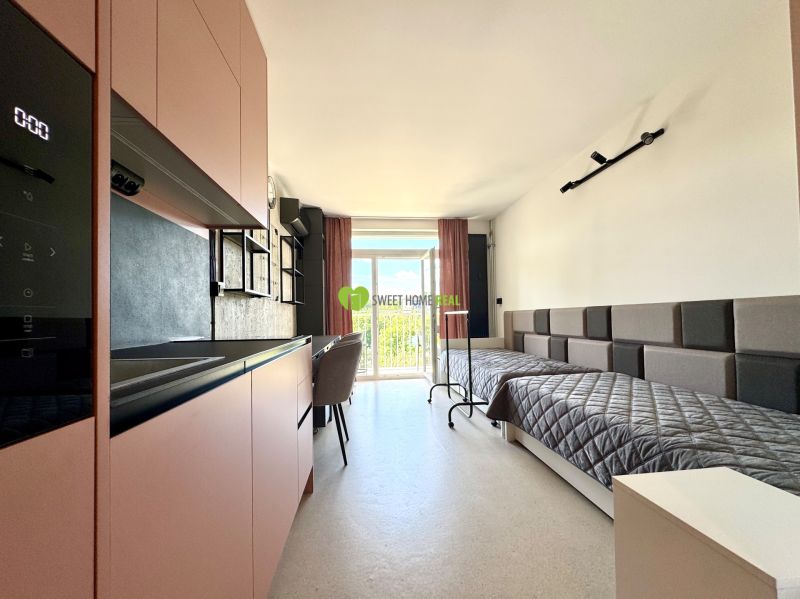 Einzimmerwohnung mit Küchenzeile und zwei Betten, Bodenbelag in Holzoptik.