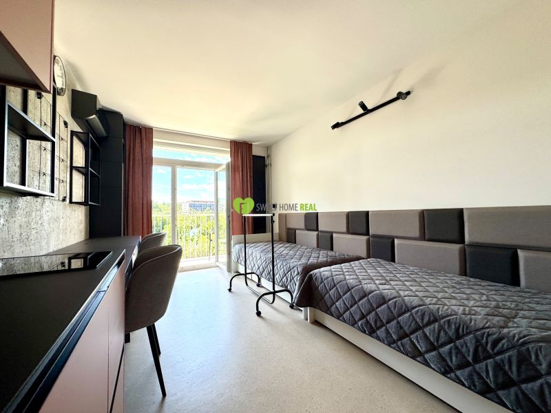 Einzimmerwohnung mit zwei Betten, einem Tisch und einem Blick durch ein großes Fenster.