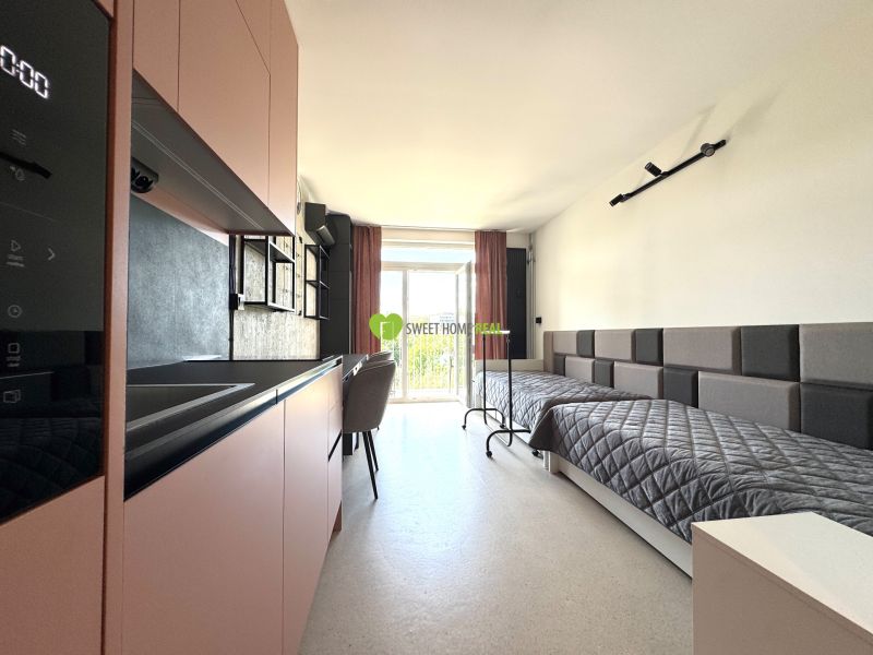 Einzimmerwohnung mit Bett, Küchenzeile und Balkontüren, Boden mit Holzdekor.