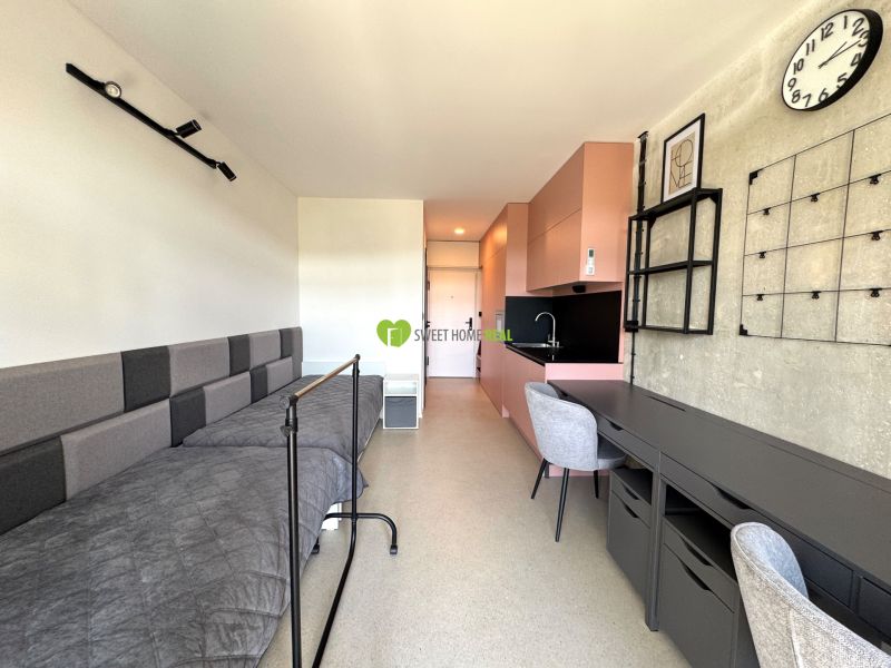 Einzimmerwohnung mit Bett, rosa Küche, Tisch und Stuhl im Innenraum.