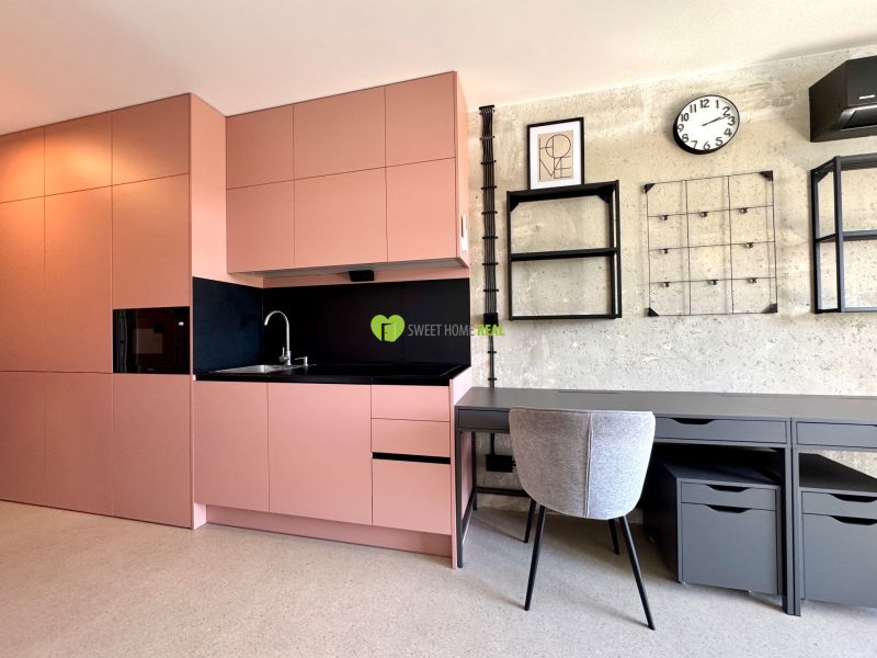 Küche und Arbeitsecke in einem Studio-Apartment mit modernen Regalen und einer Uhr an der Wand.