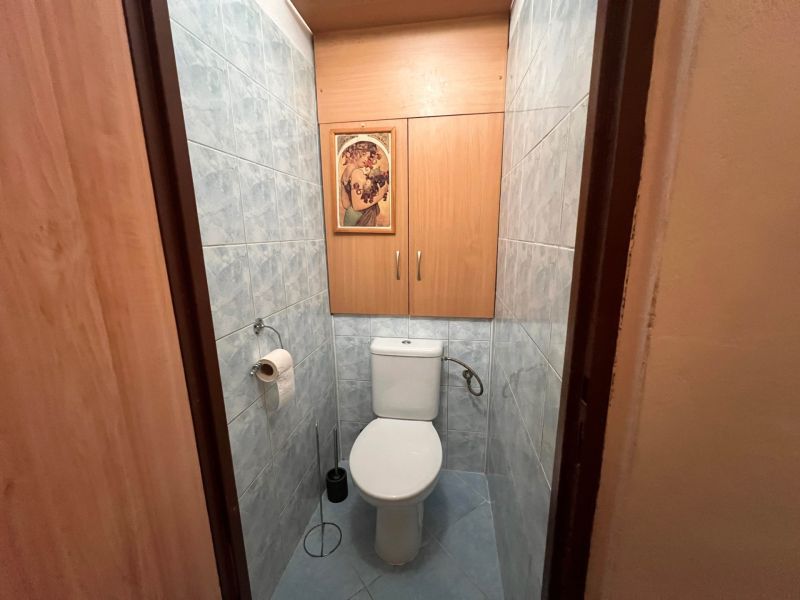 Toilette in einer 2-Zimmer-Wohnung mit blauen Fliesen und Holzdekor-Schränken.