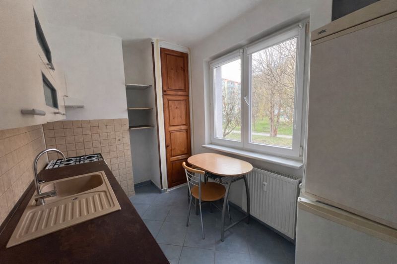 Küche in einer 2-Zimmer-Wohnung mit Holzschränken und einem Tisch am Fenster.