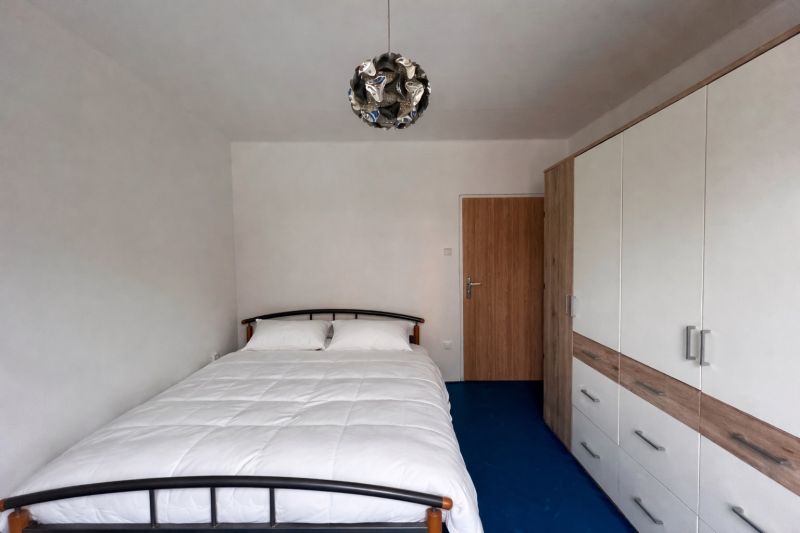 Schlafzimmer in einer 2-Zimmer-Wohnung mit Bett, Kleiderschrank und blauem Boden.