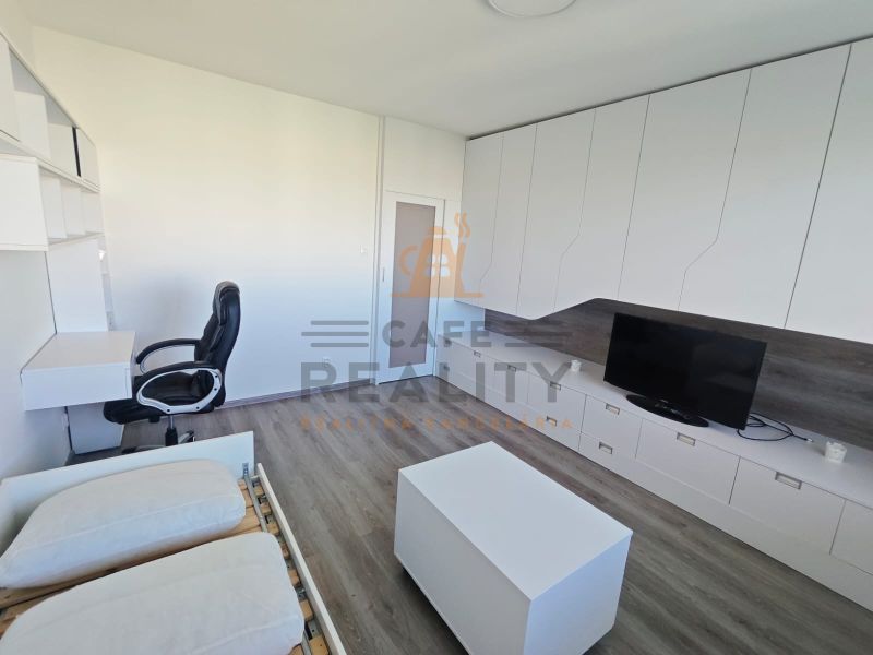 Innenraum einer Einzimmerwohnung mit Schreibtisch, Fernseher und Boden in Holzoptik.