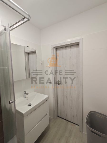 Badezimmer in einer Einzimmerwohnung mit weißem Waschbecken und Dusche, Boden mit Holzdekor.