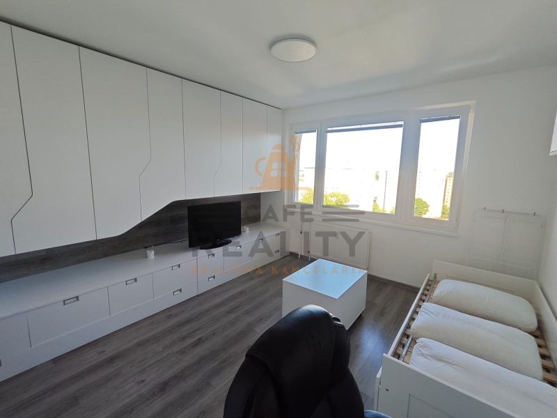 Innenraum einer Einzimmerwohnung mit weißen Schränken, Holzboden und großen Fenstern.