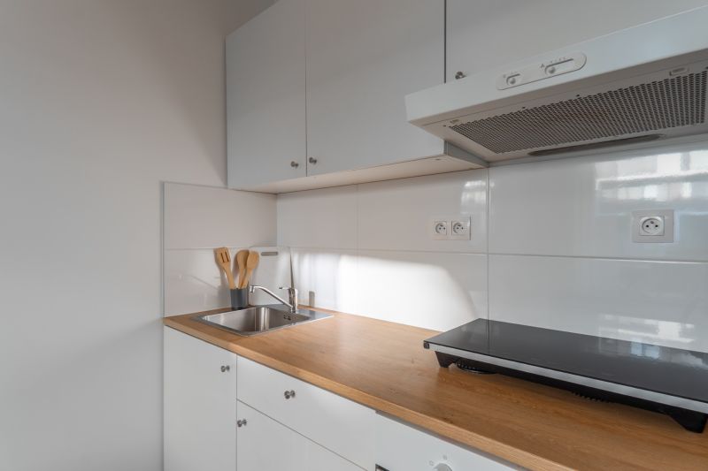 Küchenecke mit weißen Schränken, Holzelementen und Edelstahlspüle in einer Einzimmerwohnung.