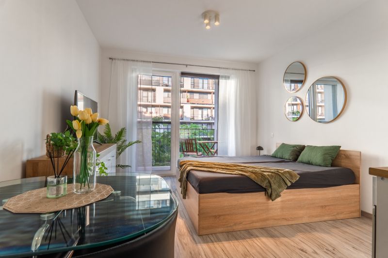 Helle 1-Zimmer-Wohnung mit Bett, Spiegeln und Holzboden, Balkon vor dem Fenster.