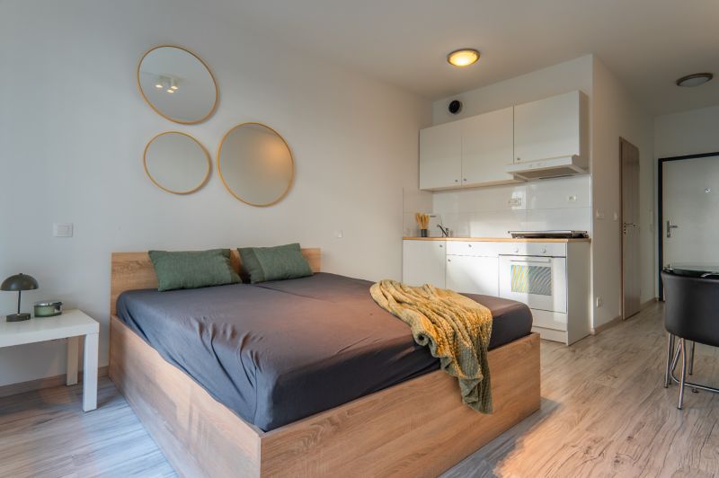 Einfaches Zimmer mit Bett, Kochnische und Boden in Holzoptik.
