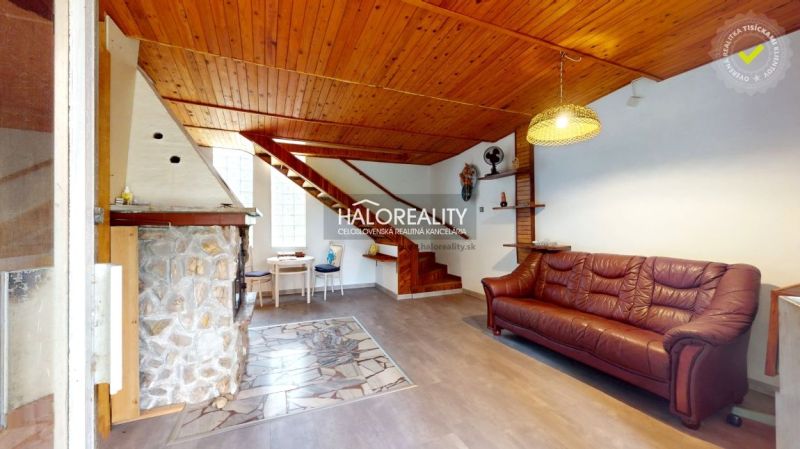 Innenraum einer Hütte mit Kamin, Holzboden und Treppe.