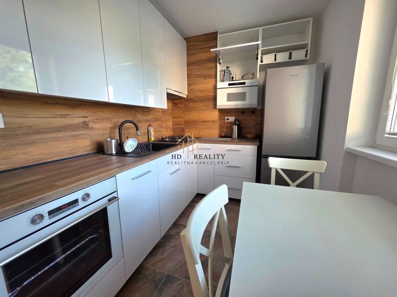 Eine Küche mit weißen Schränken und Geräten, ausgestattet mit einem Boden in Holzoptik in einer Zweizimmerwohnung.