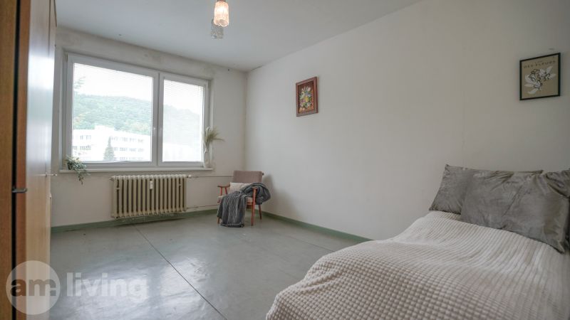Schlafzimmer in einer 2-Zimmer-Wohnung mit großem Fenster, Sessel und einfacher Einrichtung.