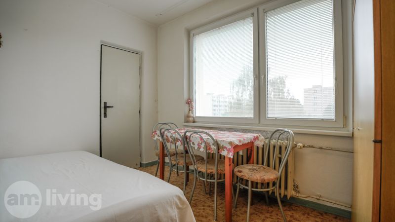 Esszimmer in einer 2-Zimmer-Wohnung mit einem Tisch mit Blumenmuster, Stühlen und großen Fenstern.