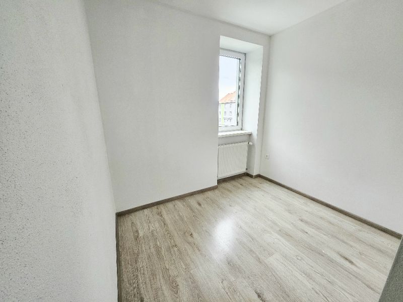 Ein Zimmer in einer Einzimmerwohnung mit einem Boden in Holzoptik und einer hellen Wand.