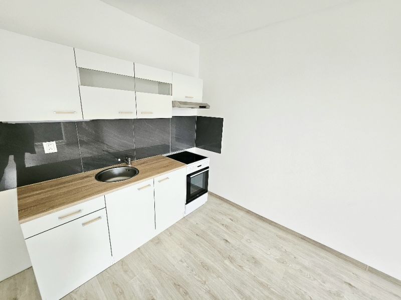 Weiße Küchenzeile mit schwarzer Verkleidung in einer Einzimmerwohnung mit Holzboden.