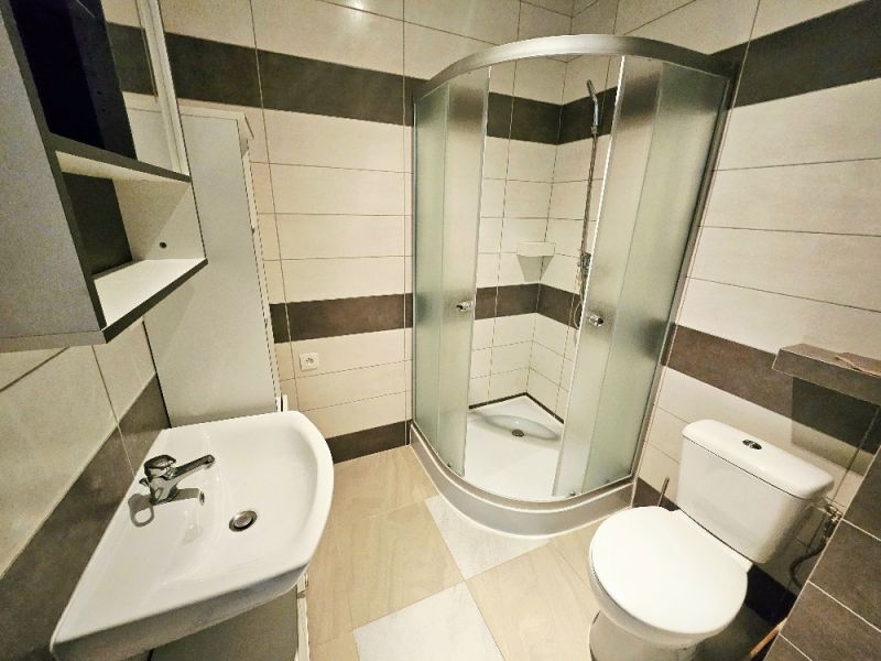 Badezimmer in einer Einzimmerwohnung mit Waschbecken, Duschkabine und Toilette.