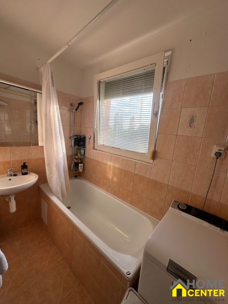 Badezimmer in einer 3-Zimmer-Wohnung mit Badewanne, Waschbecken und Waschmaschine, Fliesen in warmen Tönen.