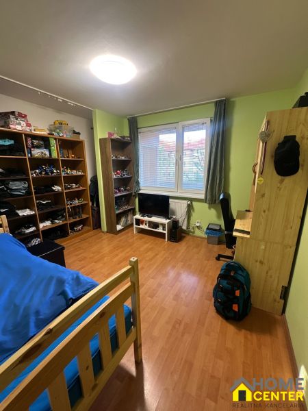 Ein Zimmer in einer 3-Zimmer-Wohnung mit Regalen, einem Bett und einem Boden in Holzoptik.