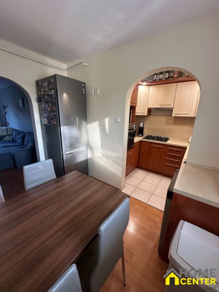 Küche mit Holzelementen, Esstisch, Kühlschrank und ein Bogen, der ins Wohnzimmer führt.