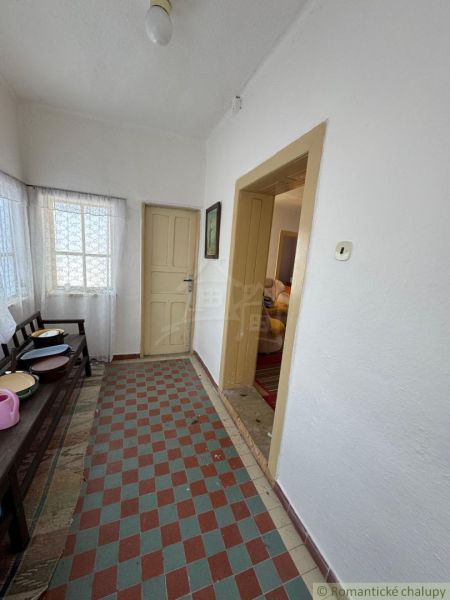 Chodba in einem Einfamilienhaus mit gefliestem Boden, weißen Wänden und einfacher Einrichtung.
