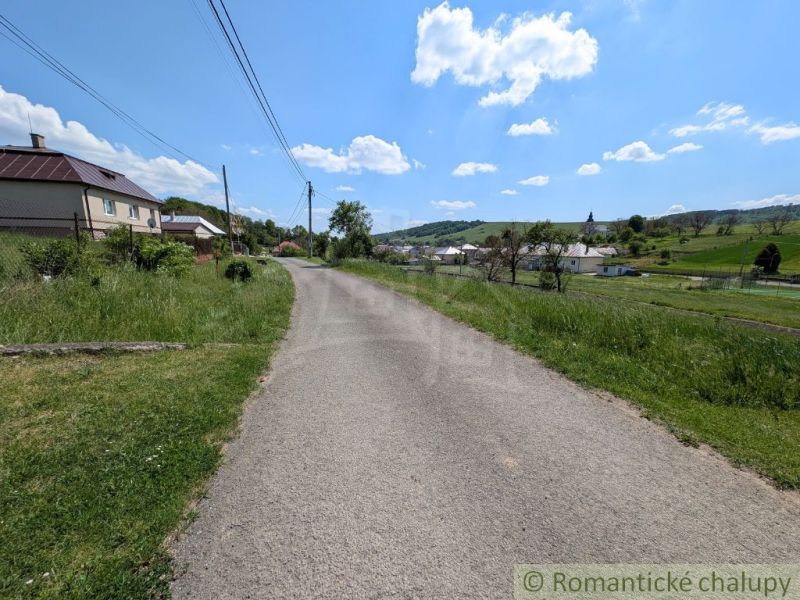 Ein von Gras umgebener Weg führt durch eine ländliche Gegend in Karna mit Blick auf Häuser.