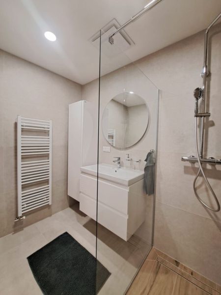 Badezimmer in einer 2-Zimmer-Wohnung mit Holzboden, Duschkabine und rundem Spiegel.
