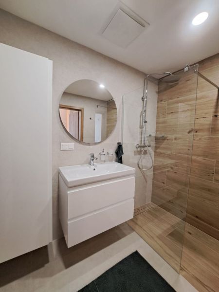 Badezimmer in einer 2-Zimmer-Wohnung mit Waschbecken, Duschkabine und Boden mit Holzdekor.
