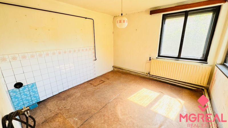 Ein unmöbliertes Zimmer mit Fenster, Heizkörper und einem Boden in Holzoptik in einem Einfamilienhaus.
