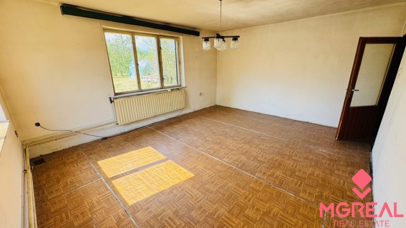 Ein Zimmer mit einem Holzboden, einem großen Fenster und einem Heizkörper in einem Einfamilienhaus.