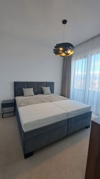 Schlafzimmer in einer 2-Zimmer-Wohnung mit Bett, Nachttisch und Vorhängen.