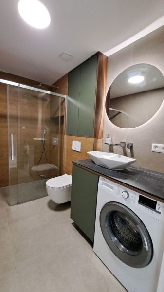 Badezimmer einer 2-Zimmer-Wohnung mit Dusche, Waschmaschine, Spiegel und Schränken in neutraler Farbe.