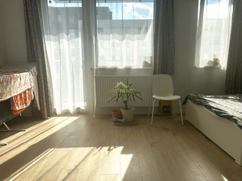 Helles Zimmer in einer Einzimmerwohnung mit Holzboden und einer Pflanze.