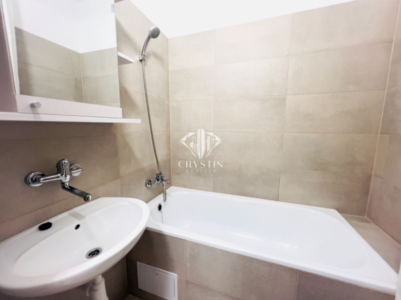 Badezimmer in einer 2-Zimmer-Wohnung mit Badewanne, Waschbecken und hellen Keramikfliesen.