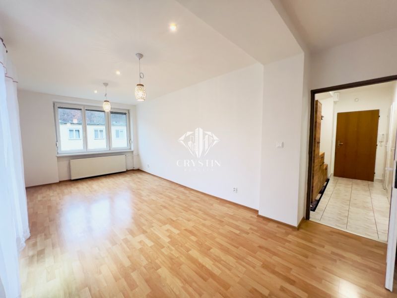 Ein Zimmer in einer 2-Zimmer-Wohnung mit Holzboden, Leuchten und einem eingebauten Fenster.