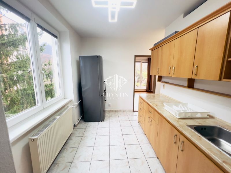 Küche in einer 2-Zimmer-Wohnung mit Fenstern, Fliesen und Holzdekor der Schränke.