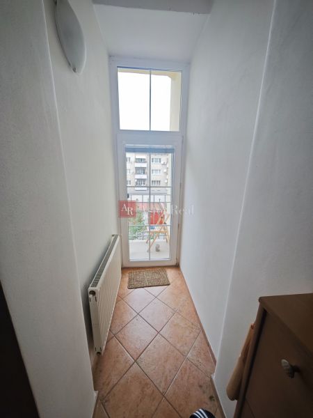 Ein schmaler Flur mit einem Fenster und einem Heizkörper in einer 2-Zimmer-Wohnung, Fliesen auf dem Boden.