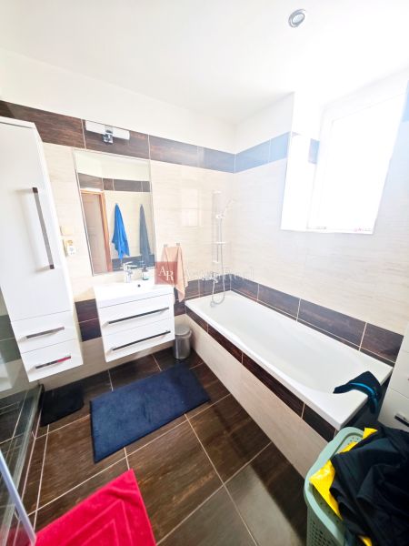 Badezimmer in einer 2-Zimmer-Wohnung mit Badewanne, Dusche und weißen Möbeln.