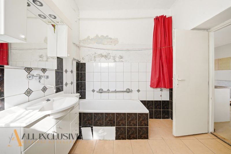Ein Badezimmer in einem Einfamilienhaus mit einer Badewanne, weißen Fliesen und einem roten Vorhang.