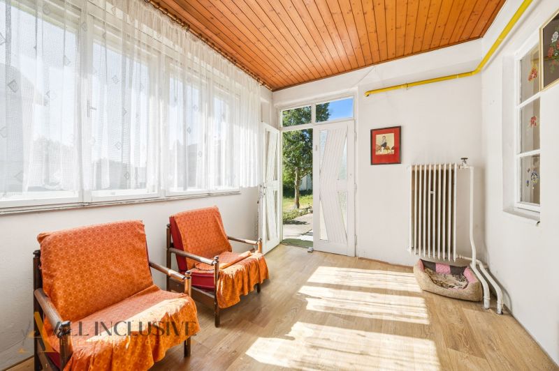 Innenraum eines Einfamilienhauses mit Sesseln, großen Fenstern und einem Boden in Holzoptik.