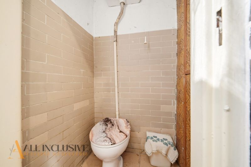 Einfaches Badezimmer mit Toilette, gefliest mit beigefarbenen Fliesen in einem Einfamilienhaus.