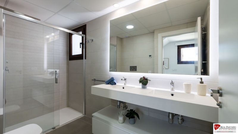 Badezimmer in einer 2-Zimmer-Wohnung mit Doppelwaschbecken, Spiegel und Duschkabine.