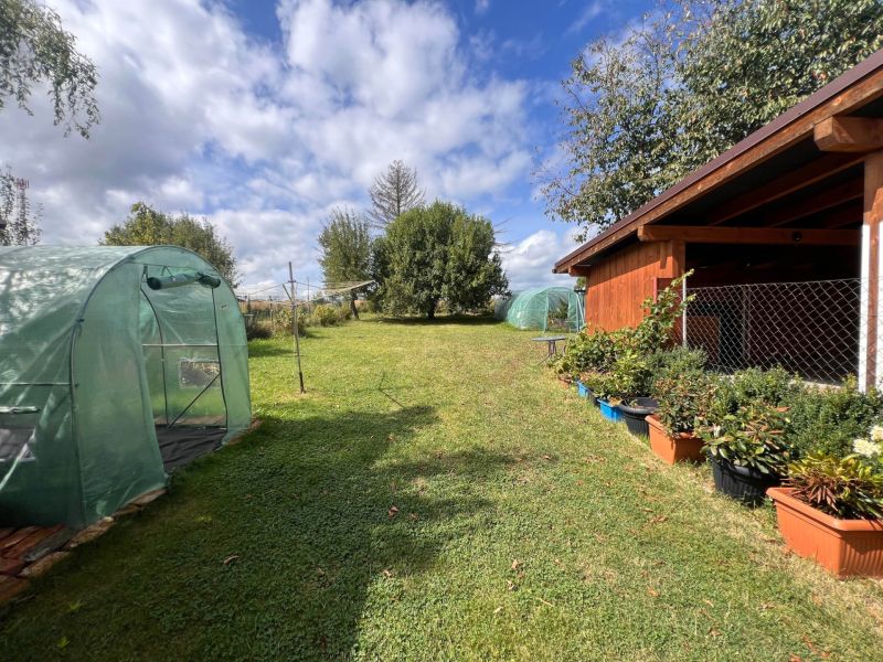 Der Garten eines Einfamilienhauses in Bacúch mit Folientunneln und einem Pavillon, umgeben von Pflanzen.
